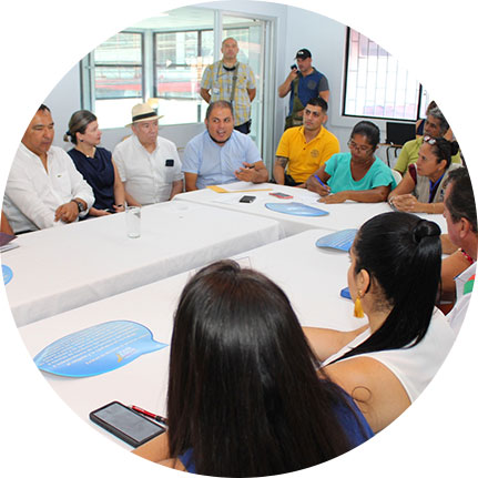 Grupo de personas reunidas, alrededor de una mesa, en una sala