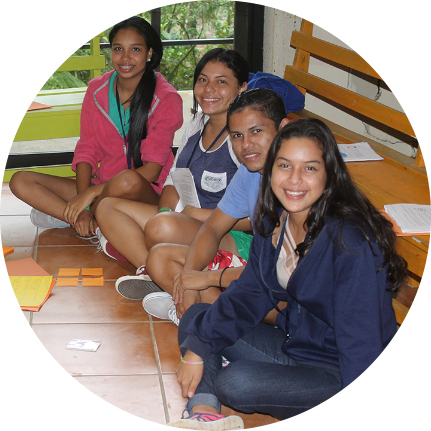 Cuatro jóvenes sentados en el piso, sonriendo, tres son mujeres y un hombre